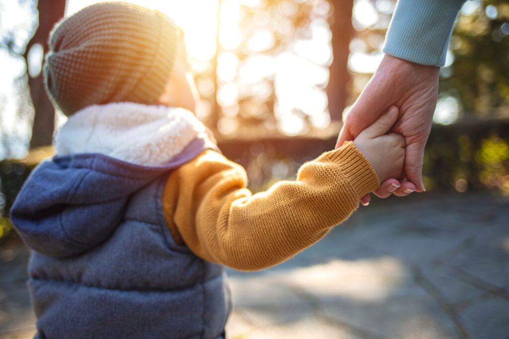 Adult holding toddler's hand on sunlit path | Hemmat Law Group