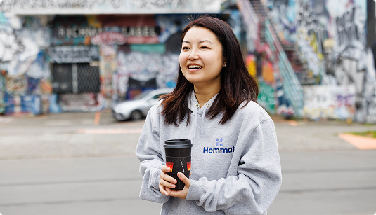 Woman in Hemmat hoodie holding coffee, street art | Hemmat Law Group